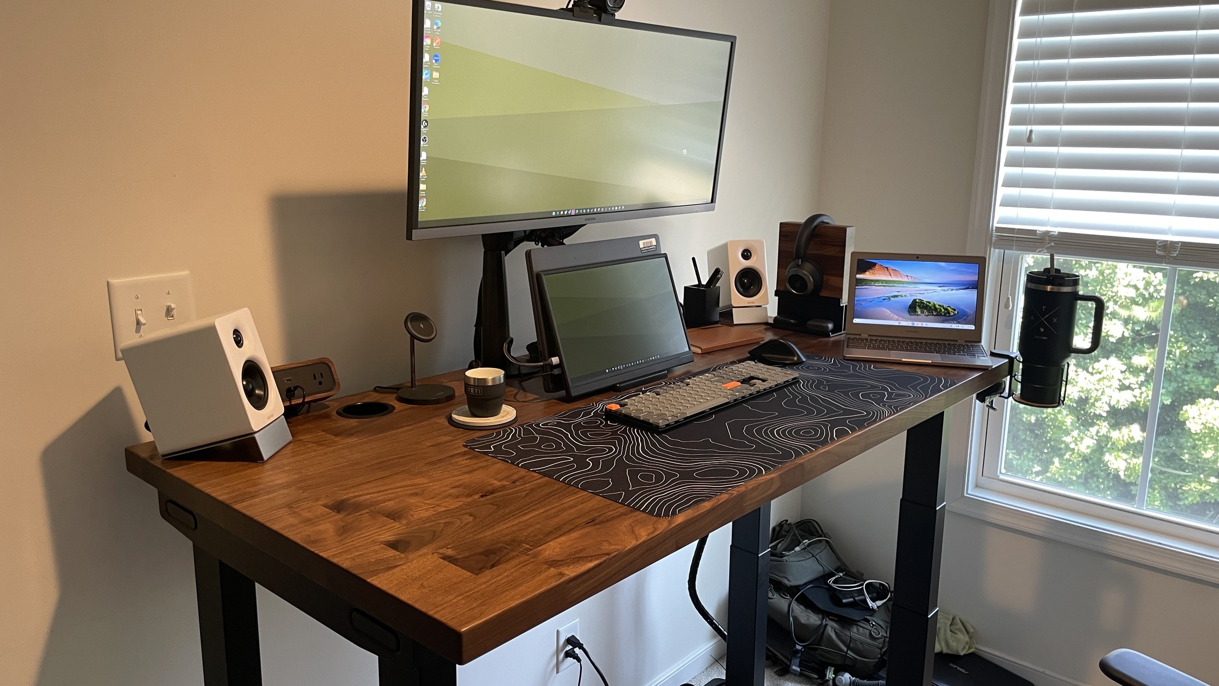 UPLIFT V3 4 Leg Standing Desk with walnut desktop, dual monitor setup, and window light